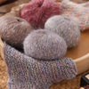 A collection of fluffy, hand-dyed alpaca blend yarn skeins in various shades of pink, gray, and beige.