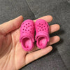 A pair of bright pink fashion slippers with perforated toes are held in a person's hand.
