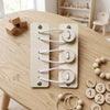 A wooden Montessori busy board for toddlers featuring gears, switches, and LED lights on a light wood table.