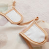 A pair of light beige waterproof baby bibs with long sleeves shown against a pale floral background.