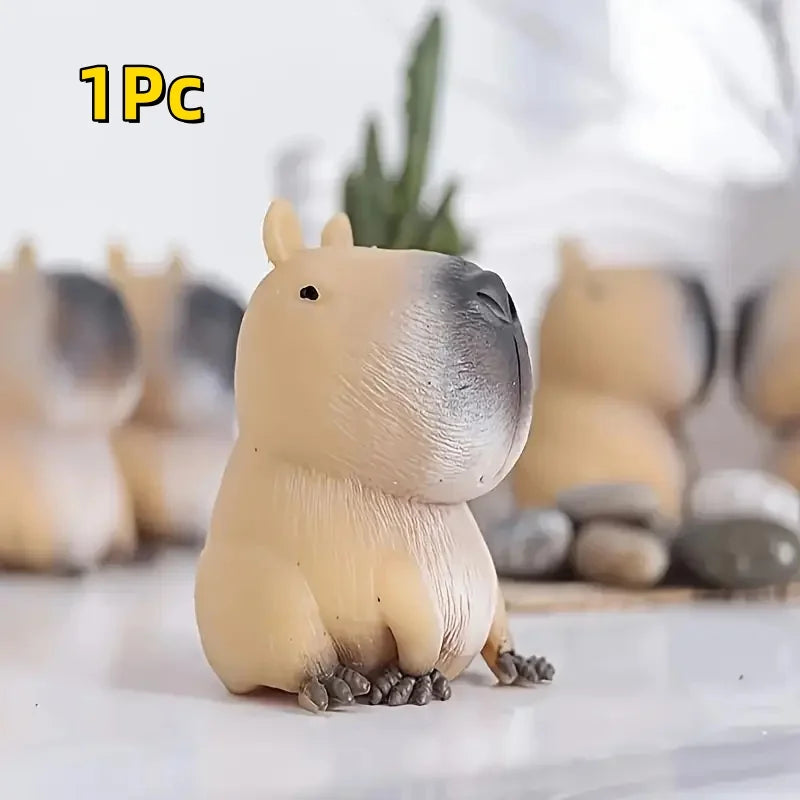 A small, light beige and gray squishy toy shaped like a capybara, resting on a white surface.