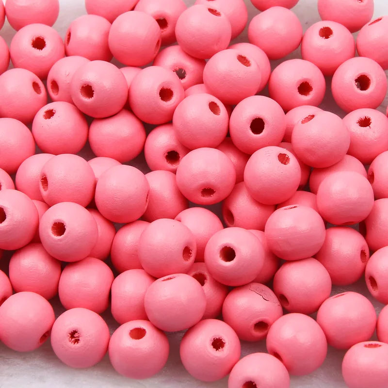 A pile of small, round pink wooden beads for jewelry making and DIY crafts.