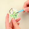 Hands use blue tweezers to apply gold and white glitter to a translucent sheet for nail art