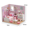 A pink miniature dollhouse kit featuring a crib, furniture, and decorative items for a kitten theme.