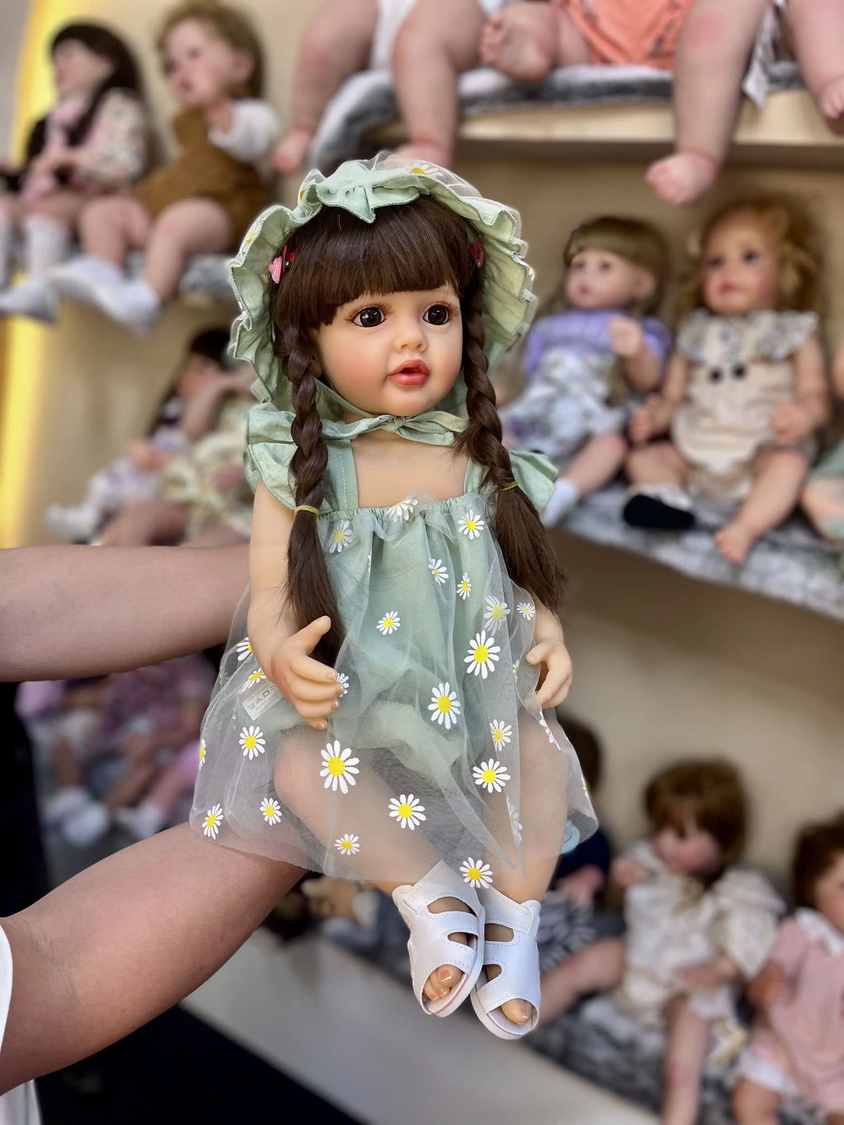 A realistic silicone vinyl toddler doll named Betty with long brown hair and a green dress sitting on a shelf.