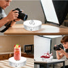 A person is using a camera near a round, white motorized display stand for a product.