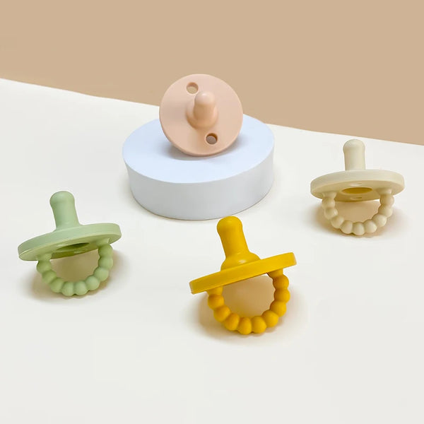 A set of food grade silicone baby pacifiers and a white silicone soother displayed on a light surface.