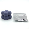 A small pile of purple candle dye chips for wax, next to a sealed plastic bag.