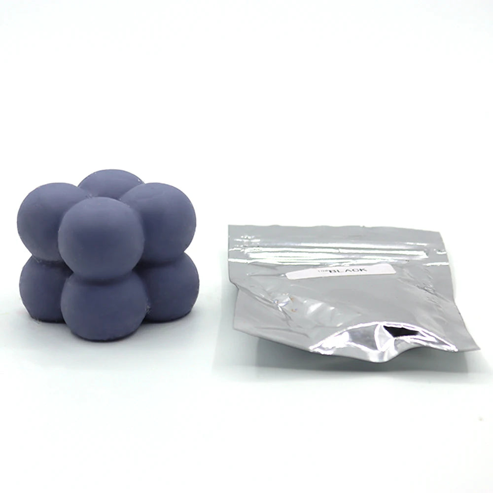 A small pile of purple candle dye chips for wax, next to a sealed plastic bag.