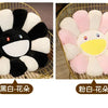 Two plush sunflower cushions, one black and white, and one pink and white, displayed on a gold wire tray.