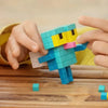 Hands are assembling a blue and yellow Lego minifigure model on a wooden surface.