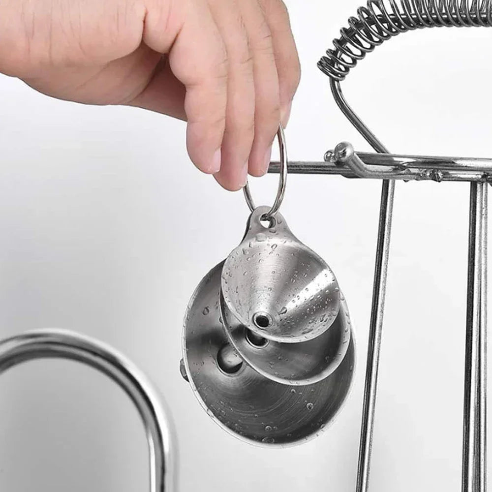 A hand is holding a stainless steel funnel with a loop attached, hanging from a wire rack.