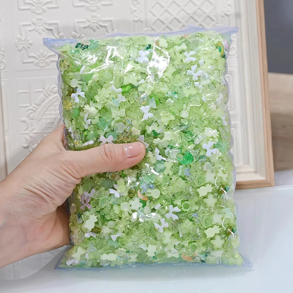 A hand holds a clear plastic bag filled with multicolor aurora mix resin nail charms.