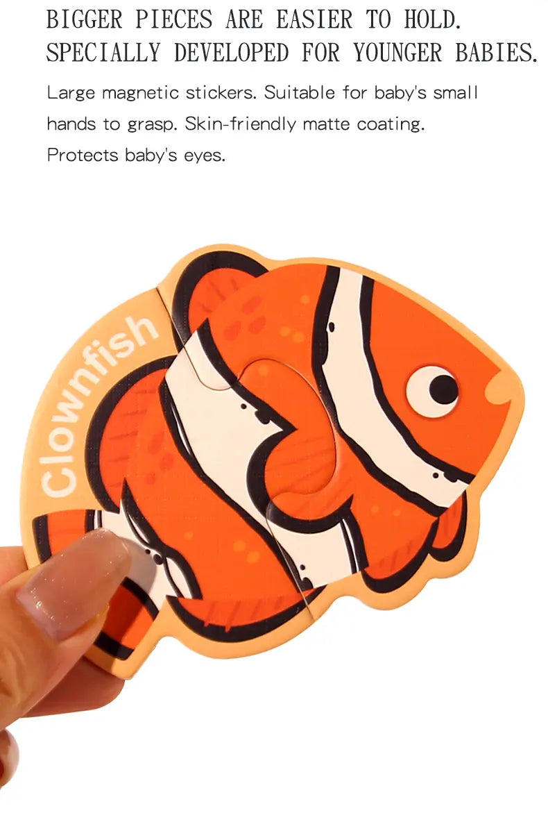 An orange clownfish magnetic puzzle piece with black stripes and white accents being held by a hand.