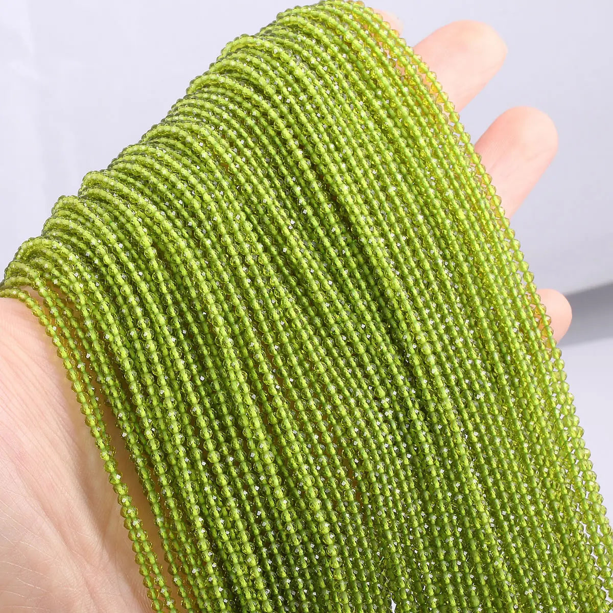 A hand holds a strand of bright lime green faceted natural stone beads for DIY jewelry making