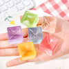 A hand holds several colorful ice cube squishy fidget toys on a white surface.