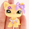 A small yellow cat figure with purple accents and a lavender bow is held in a person's hand.
