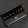 A set of six green polyhedral dice in a black box with a gold mini planet logo on the exterior.