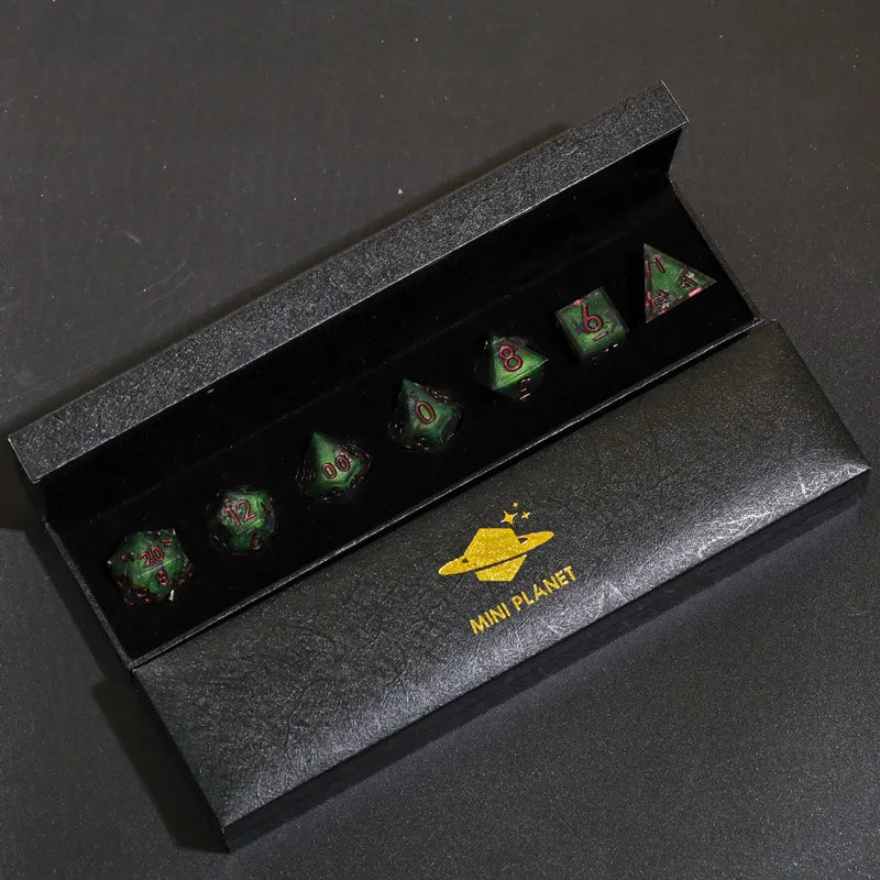 A set of six green polyhedral dice in a black box with a gold mini planet logo on the exterior.