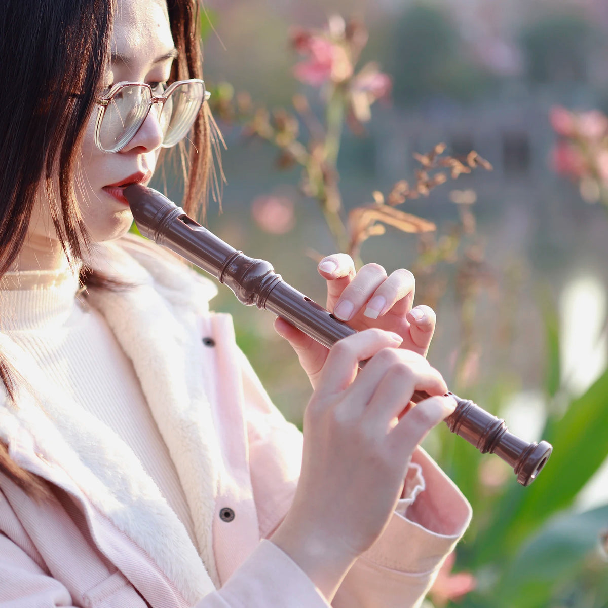 A young woman holds an 8-hole soprano recorder for kids and beginners outdoors.