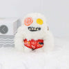 A white fluffy monster plush toy with yellow eyes and orange markings, featuring a stitched mouth and a red decorative band.