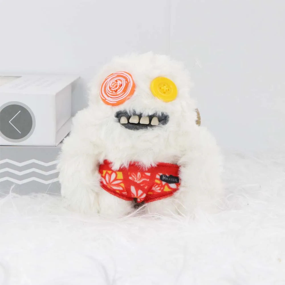 A white fluffy monster plush toy with yellow and orange eyes and a stitched mouth, resting on a white surface.