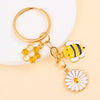 Gold enamel keychain featuring a bee and a daisy flower design.