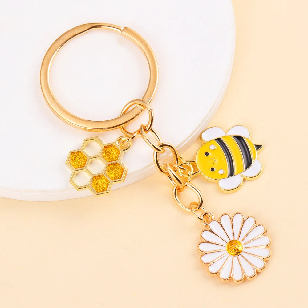 Gold enamel keychain featuring a bee and a daisy flower design.