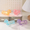 Trois jouets stress-relief en forme de chiens dachshund scintillants, orange, rose et violet, sont exposés sur une surface bl