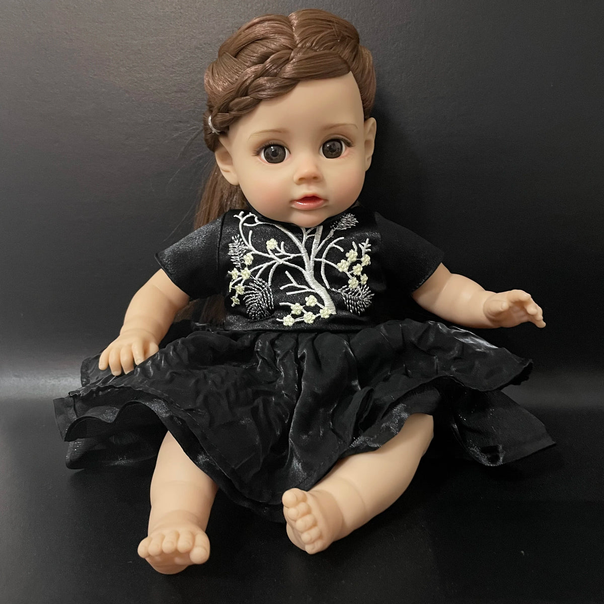 A lifelike 14-inch reborn baby doll with a dark outfit and natural skin tone.