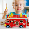A toddler holds a red wooden toy vehicle with yellow accents and various tools like a screwdriver and wrench.