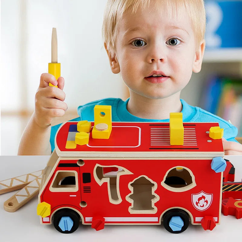 A toddler holds a red wooden toy vehicle with yellow accents and various tools like a screwdriver and wrench.