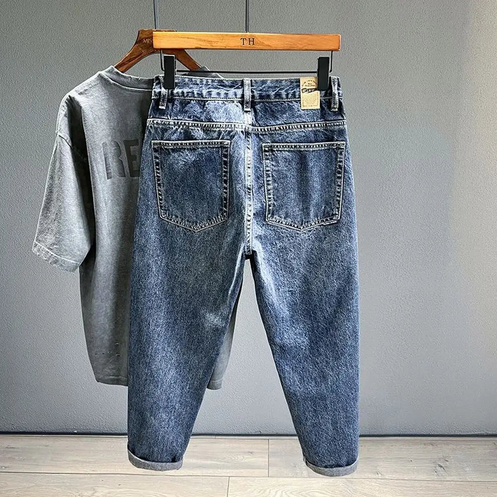 A pair of dark blue vintage loose fit denim harem jeans hanging on a wooden hanger.