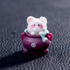 A small white cartoon bear figurine with pink accents is sitting in a purple pot.