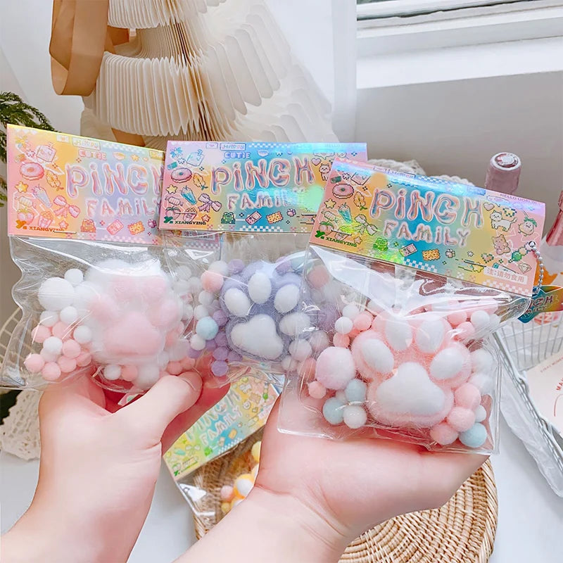 Hands holding clear bags of pink and purple cat paw squishy stress relief toys