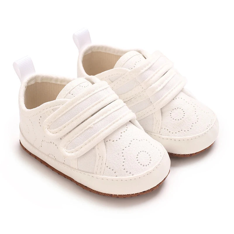 A pair of classic white soft-sole baby first walkers with elastic straps shown from the side.