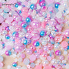 A close-up of mixed resin rhinestone pearls in various shades of pink, blue, and iridescent colors scattered on a surface.