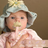 A baby wearing a light blue knitted hat with a flower, holding a silicone teething toy.