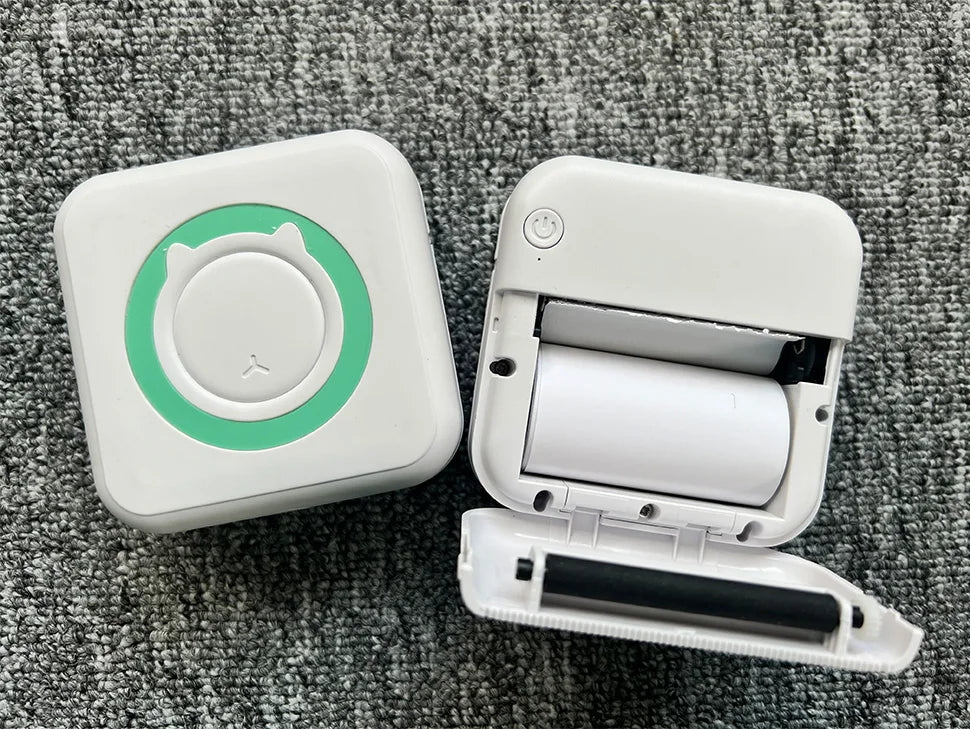 A white pocket thermal printer is shown open, displaying the roll of paper inside, set against a gray fabric background.