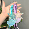 A hand holds a set of beaded keychains featuring starfish and seashell charms in shades of blue, purple, and pink.