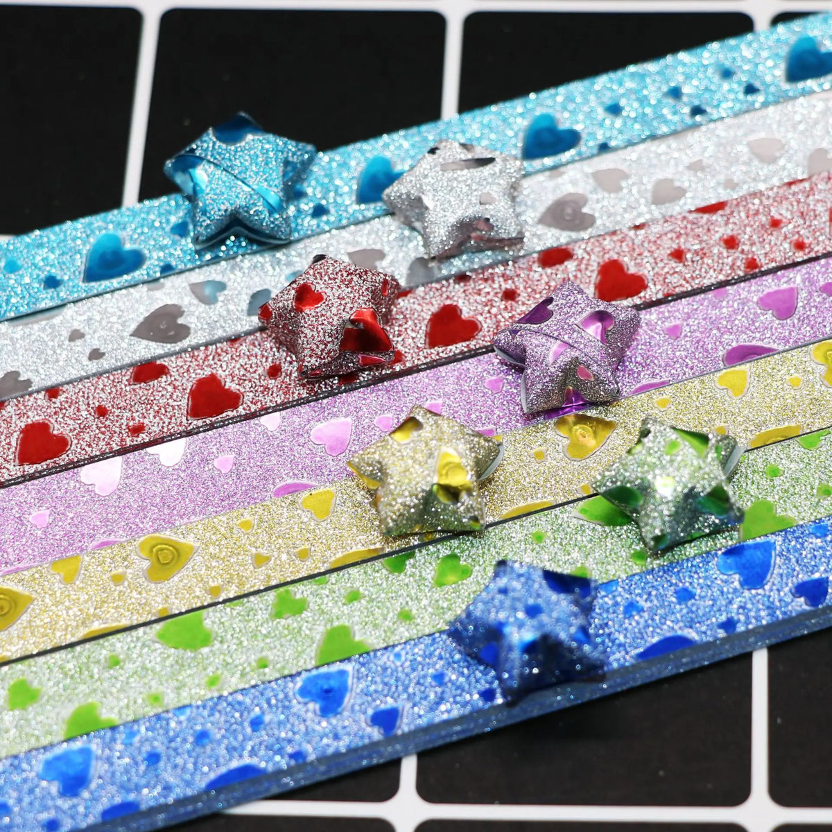 Colorful glitter origami star paper strips arranged in horizontal strips for crafting and decorating