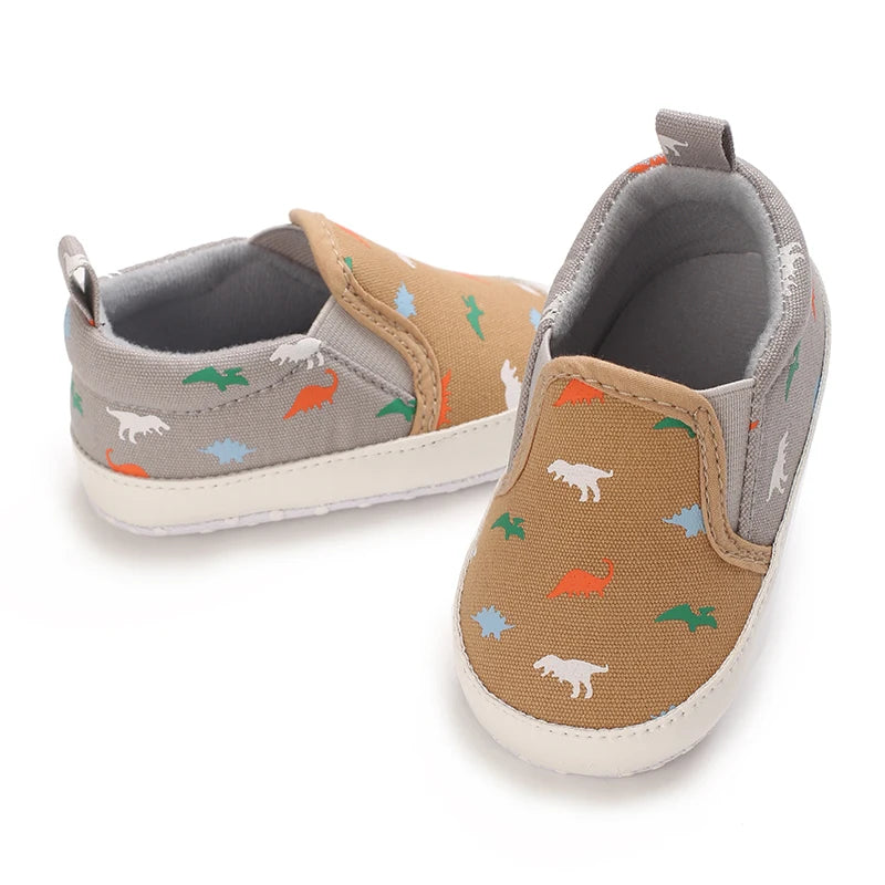 A pair of baby first walker sneakers with a dinosaur print featuring orange, green, and blue dinosaurs.