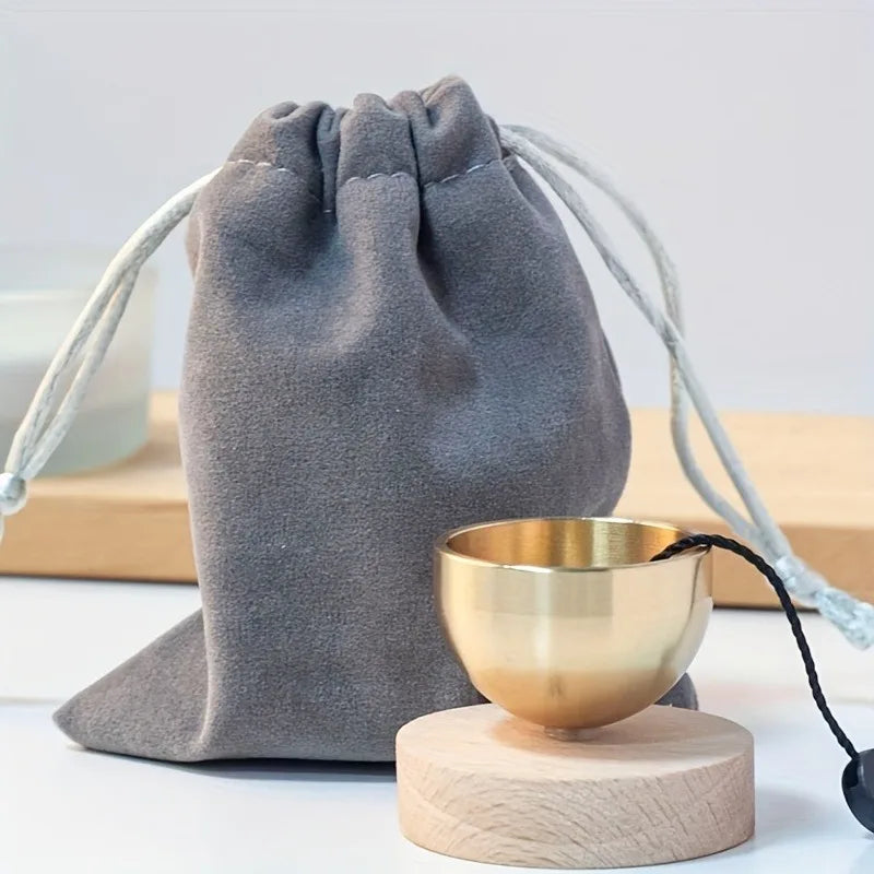 A gray fabric hand-shaped meditation pouch with white cord is shown next to a small brass singing bowl on a wooden base.