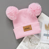Pink knitted baby beanie hat with fluffy pink pom-poms and a brown label