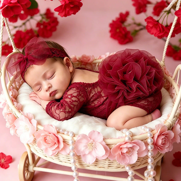 A newborn baby sleeping in a wicker basket decorated with pink flowers and pearls, wearing a red lace princess tutu dress.