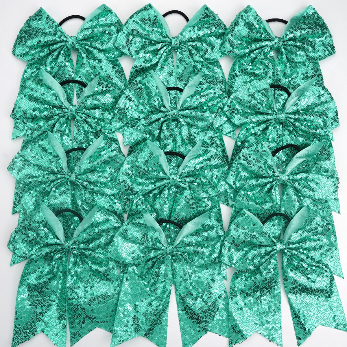 A pack of twelve teal green glitter sequin pigtail bows for girls with elastic hair ties.