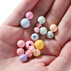 A hand holds various matte acrylic round beads in pastel colors like pink, blue, green, and yellow.