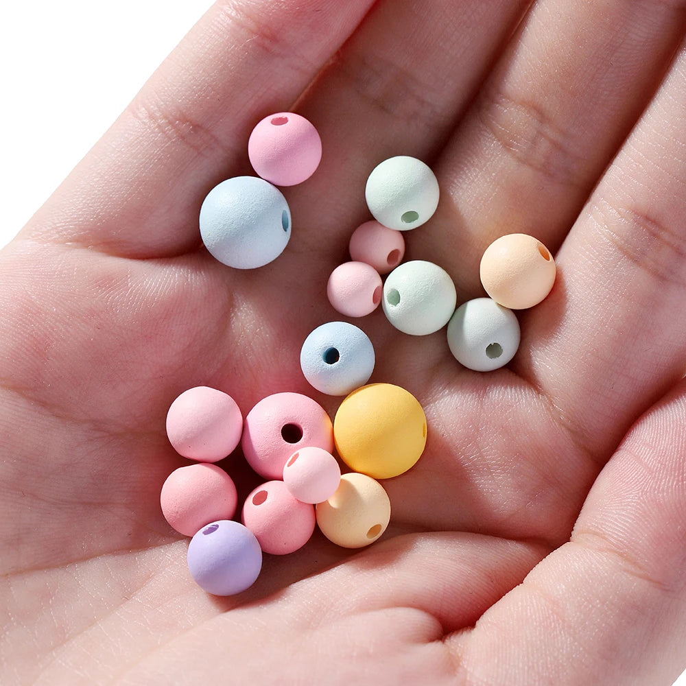 A hand holds various matte acrylic round beads in pastel colors like pink, blue, green, and yellow.