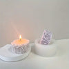 A white silicone rose candle mold with a lit candle and a molded rose flower resting on a white surface.