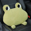 A light green plush pillow shaped like a frog with large eyes resting on a black car seat.